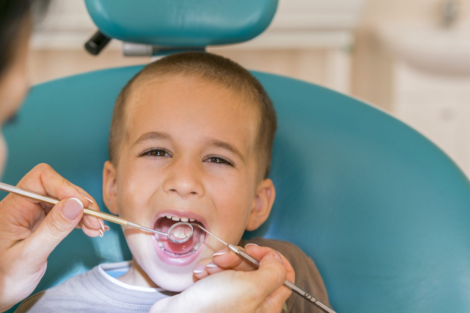 Pediatric Dentist Examining A Little Boys Teeth In The Dentists Chair At The Dental Clinic. Dentist Examining Little Boy's Teeth In Clinic